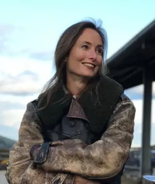 A woman wears a furred collared jacket outside and smiles