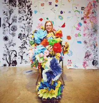 A young blonde woman covered in colourful paper flowers smiles