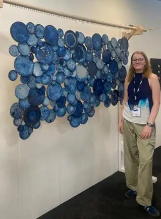 A young female student stood next to her artwork