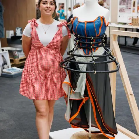 A young woman stands next to a dress she's designed out of waste festival tents