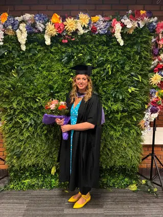 Charlene at graduation in gown holding flowers