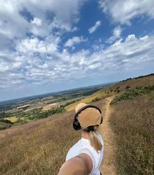 The back of a young woman's head as she faces green hills filled with heather