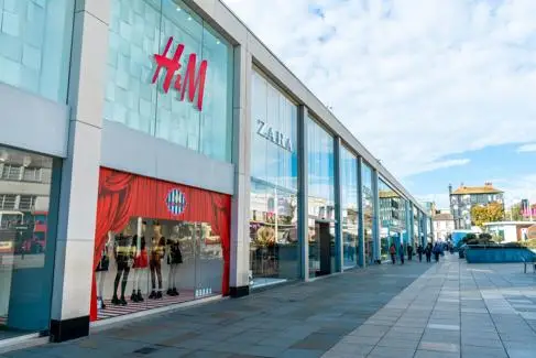 The exterior of a UK shopping centre, with HM and Zara and shoppers walking