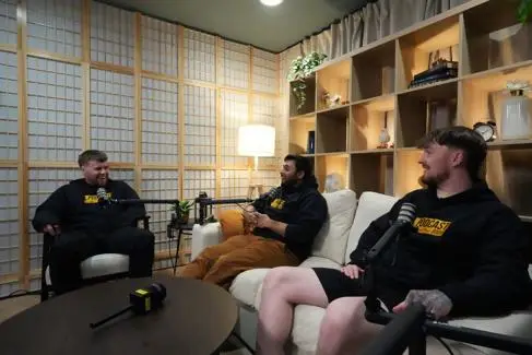 Three young men sit on sofas and armchairs, making a podcast