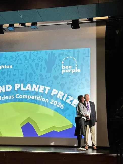 Two people smile on stage in front of a screen reading 'People & Planet Prize'