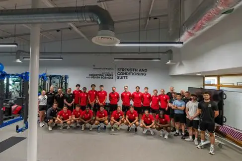Worthing football team and coaches stood in front of University of Brighton signage