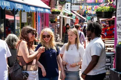 Young group of students smile, chatting in busy, colourful Brighton street
