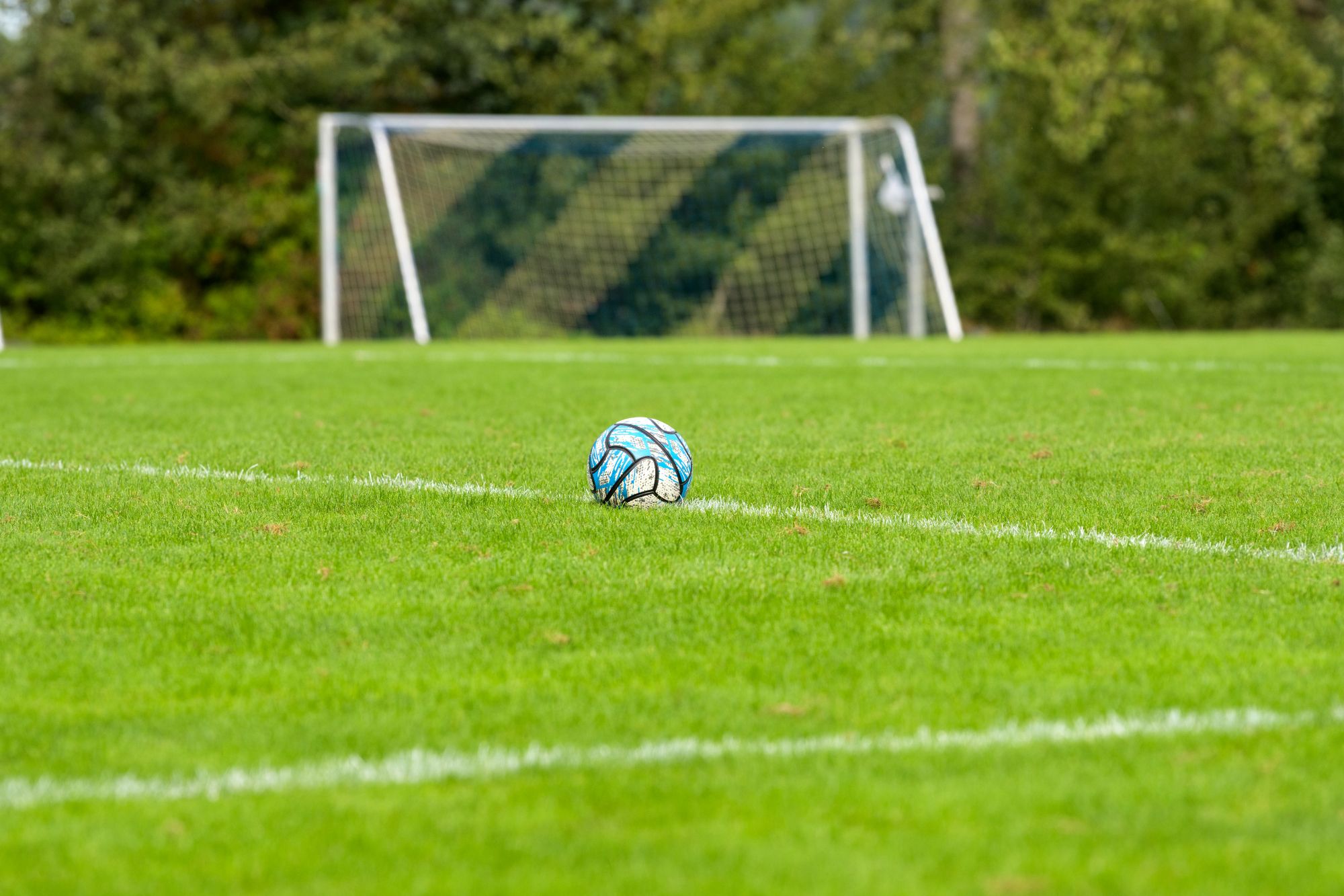 A football sits alone in a football field, in front of an empty goal