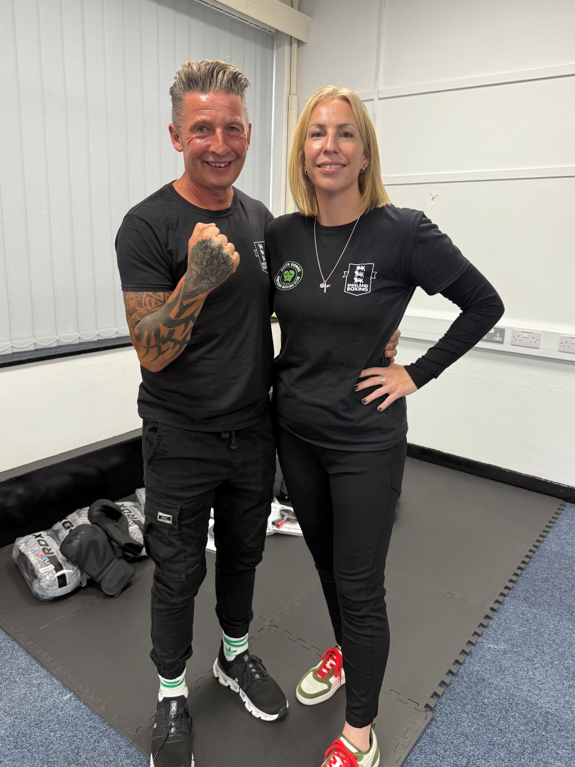 A man and a woman in gym clothes smile at the camera
