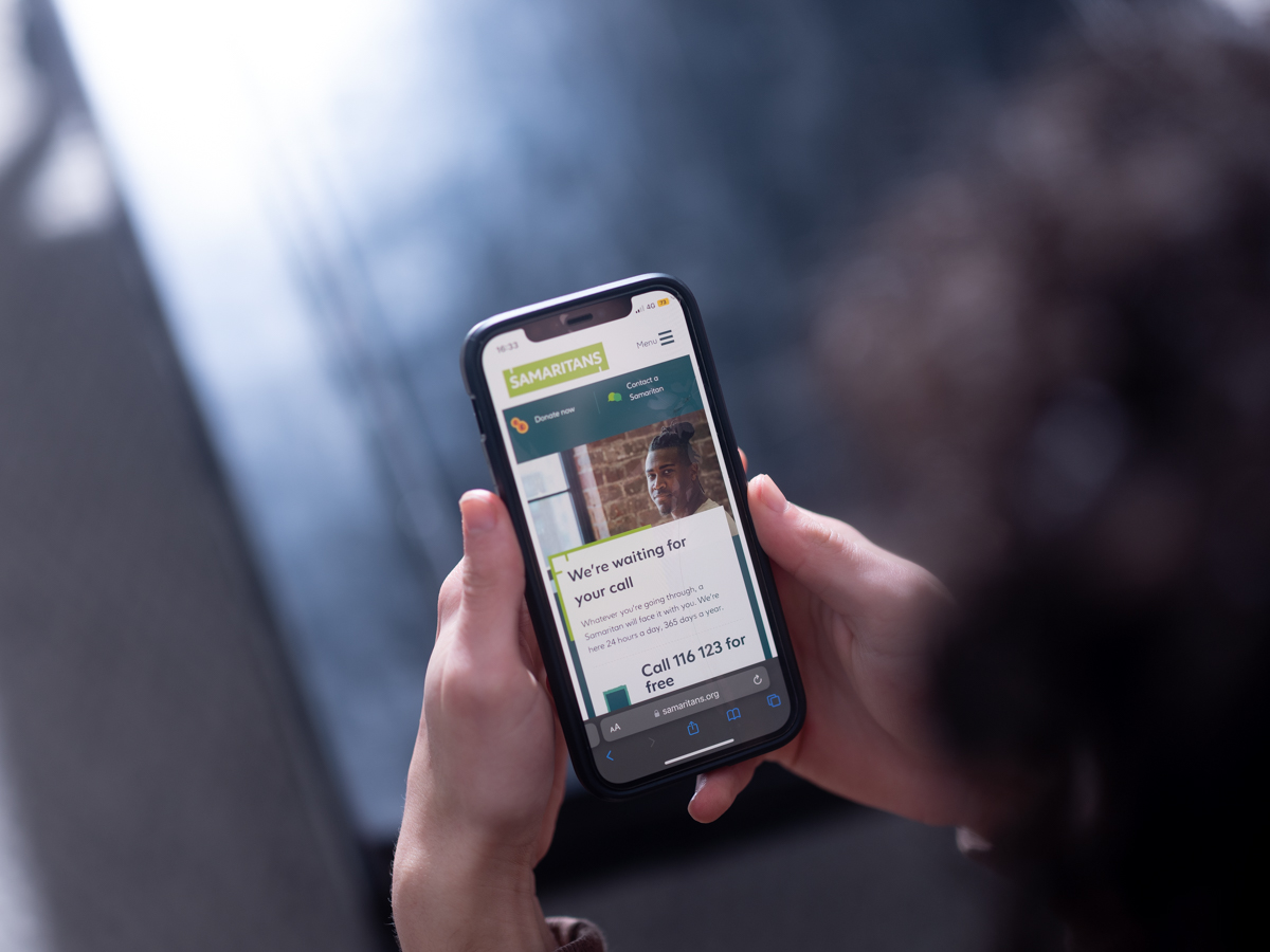 Hands holding a phone that shows the Samaritans helpline number