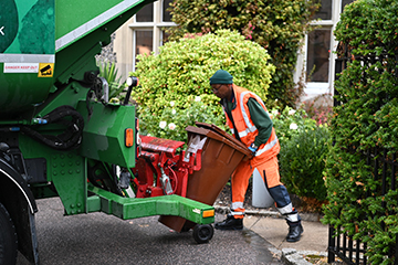 Man loading wheelie bin into truck