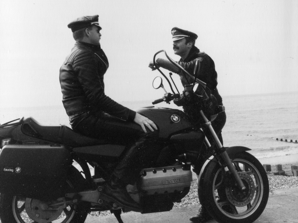 Two men in leather, one sitting astride a motorbike
