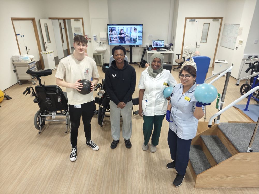 Two university students stand next to two physiotherapists on a NHS stroke ward