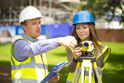Man in hardhat assisting woman in hardhat using a level