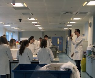 Students and lecturer wearing white coats in a lab setting