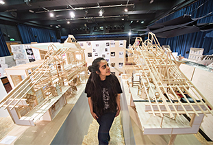 A student walking through a hall full of architectural models