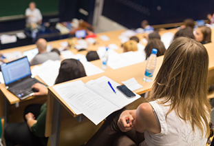 A student sitting in a lecture, with a notepad open in front of them