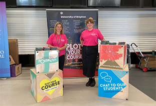 Two staff members in front of a University of Brighton stall at a higher education fair
