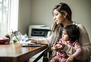 A mature student working at a laptop, holding their child