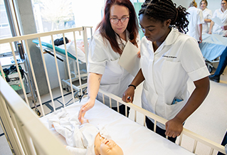 Two nursing students interacting with a dummy baby in a cot