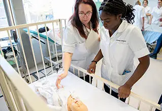 Two nursing students interacting with a dummy baby in a cot