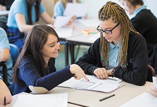 A teacher sits with a senior student in a classroom