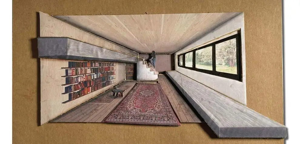 cardboard model of a long, narrow room with built-in seating, bookshelves, and a large window letting in natural light.