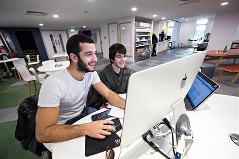 Two students working with a desktop computer and a laptop