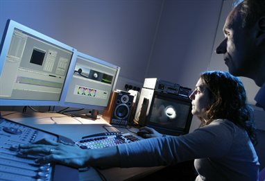 Two people in a media lab, one adjusting volume controls